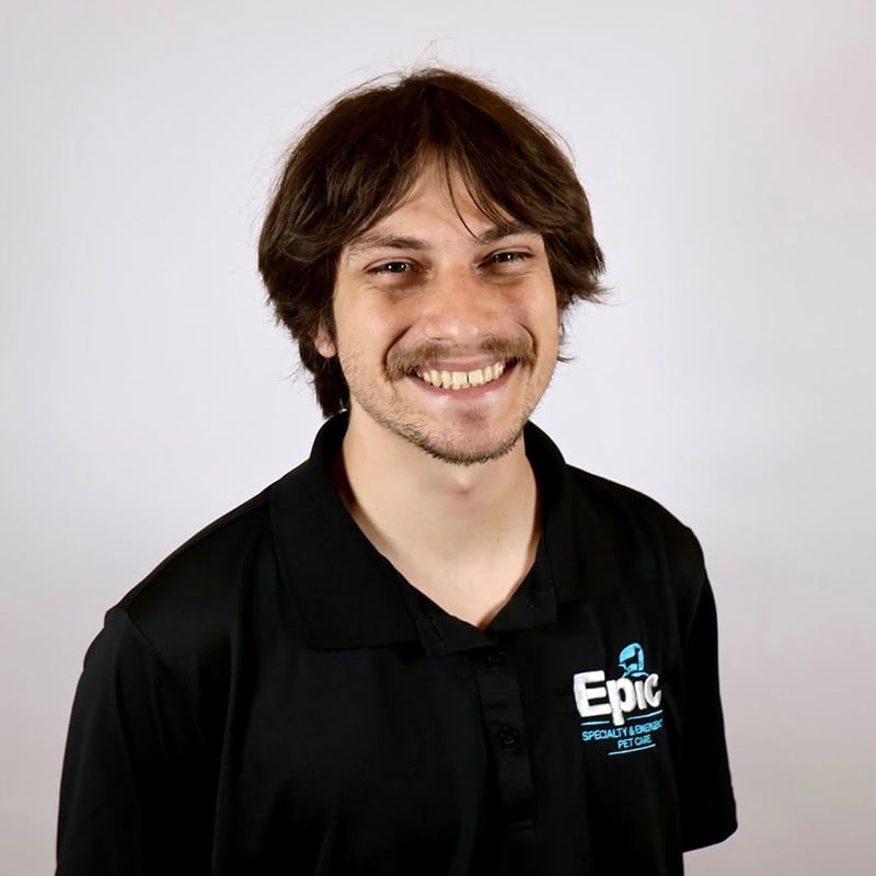 Smiling person with brown hair in a black polo shirt with an “Epic Specialty Coffee” logo, posing in front of a plain white background.