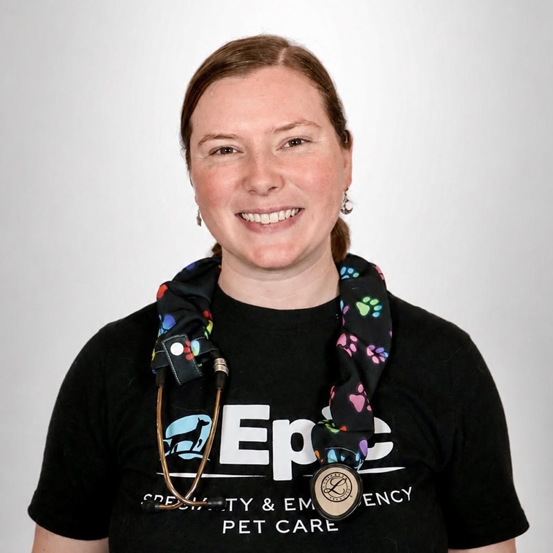 A woman smiles at the camera, wearing a black “EPEC” T-shirt and a stethoscope with a colorful paw print cover around her neck, against a plain white background.